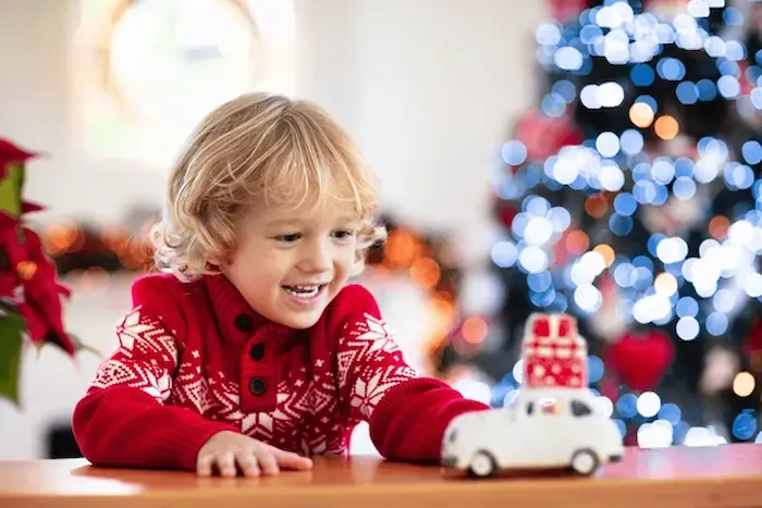 a young boy in a festive sweater smiles with glee as he plays with his christmas gift